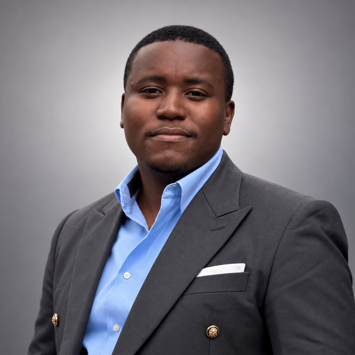 Portrait of Kudakwashe Verah in a charcoal double-breasted jacket and light blue shirt
